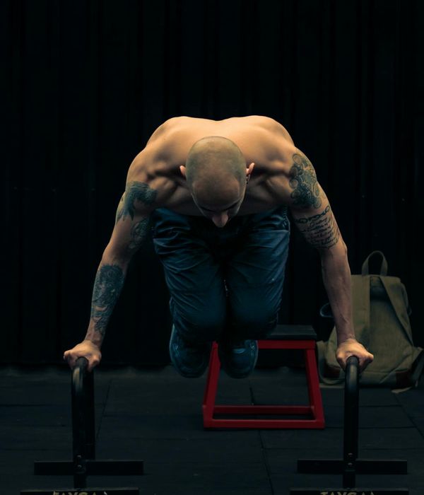 Man performing a complex bodyweight strength exercise in a dark gym.